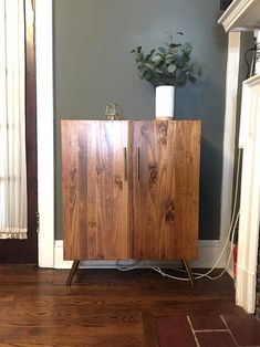 a wooden cabinet sitting on top of a hard wood floor next to a potted plant