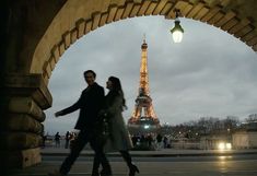 a man and woman walking under an arch in front of the eiffel tower