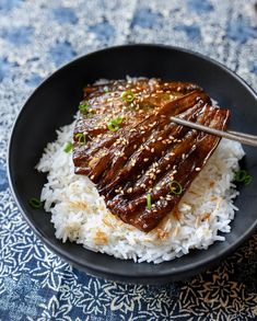 a black plate topped with rice and meat on top of a blue table cloth next to chopsticks