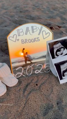 a baby's photo and shoes are on the sand at the beach with an easel next to it