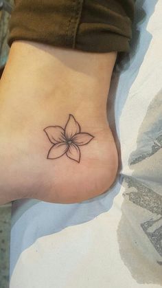 a small flower tattoo on the foot of a woman's left leg, with her right