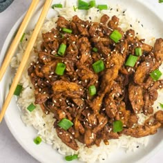 a white plate topped with meat and rice next to chopsticks on a table