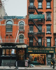 people are walking on the sidewalk in front of shops and apartment buildings with fire escapes