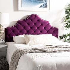 a bed with a purple headboard in a white room next to a potted plant