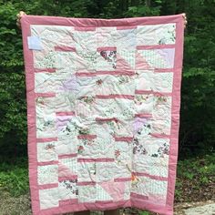 a woman holding up a pink and white quilt