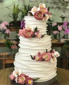 a three tiered white cake with pink flowers on the top and bottom, sitting on a wooden table