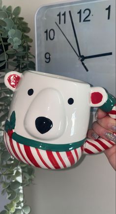 a hand holding a coffee mug with a bear face on it and candy canes in front of a clock