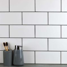 two toothbrushes are sitting in cups on the counter next to a white brick wall