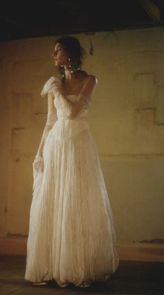 a woman in a long white dress standing on the floor with her hands behind her back