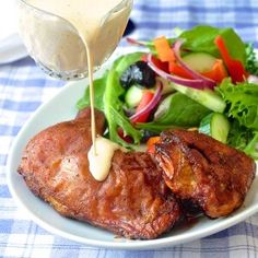 a white plate topped with meat and salad next to a glass of dressing on top of a table