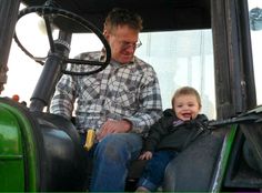 a man sitting on the back of a tractor next to a little boy