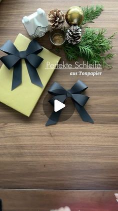 two present boxes with black bows and pine cones on the table next to each other