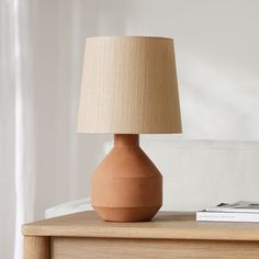 a table lamp sitting on top of a wooden dresser next to a book and magazines