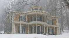 a large house in the middle of winter with snow falling on it and trees around