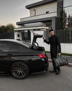 a man in a suit and tie standing next to a black car with its trunk open