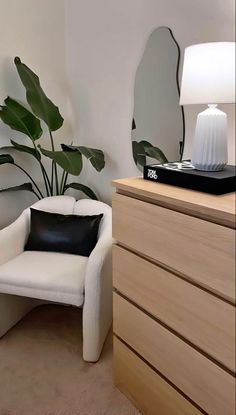 a white chair sitting in front of a mirror next to a dresser with a lamp on top of it