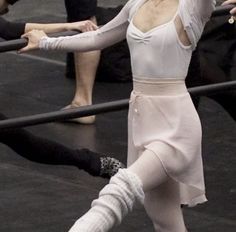 a woman in white shirt and pink skirt dancing on stage with other people behind her