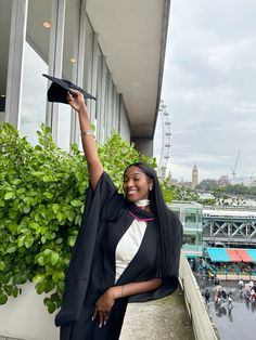 a woman in graduation gown holding up her cap on top of a balcony overlooking the city