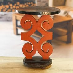 a wooden table with a metal top and decorative design on the base, in front of a living room