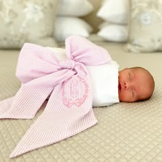 a baby wrapped in a pink bow laying on top of a bed