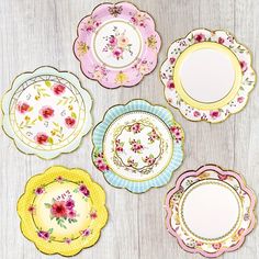 four plates with flowers painted on them sitting on a wooden table next to each other