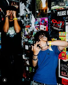 two young men standing next to each other in front of a wall covered with posters