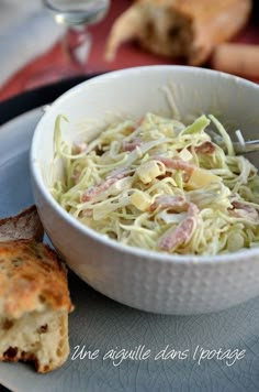 a white bowl filled with food on top of a plate next to bread and wine glasses