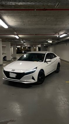 a white car is parked in an empty parking garage with no one around it and the lights on