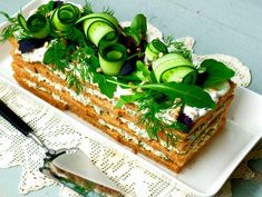 a cake with cucumbers and herbs on top is sitting on a white plate