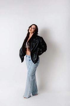 a woman in jeans and a leather jacket posing for the camera with her hands on her hips