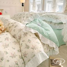 a bed with white and green comforters on top of it next to a window