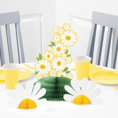 a white table topped with yellow plates and cups filled with flowers on top of it