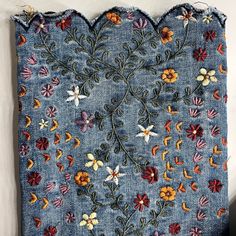 an old piece of cloth with flowers and leaves embroidered on the side, hanging up against a wall