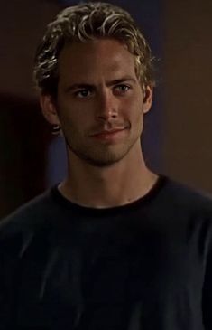 a man with blonde hair wearing a black t - shirt and looking at the camera