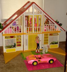 there is a doll house with a pink car in front of it and a dog on the floor