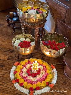 three metal bowls filled with flowers on top of a wooden floor next to a candle