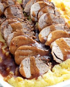 sliced meat and gravy on top of mashed potatoes in a white dish