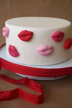 a white cake with red and pink decorations on it's side next to a red ribbon