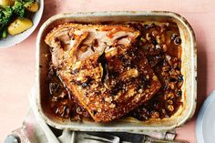 a pan filled with meat and vegetables on top of a pink table cloth next to silverware