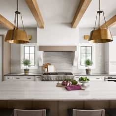 a kitchen with white counter tops and gold pendant lights hanging from the ceiling above it