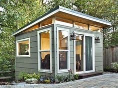 a small gray house sitting on top of a brick patio next to a wooden fence