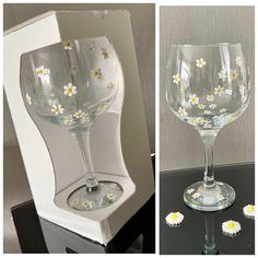 two wine glasses with daisies on them sitting next to each other in front of a box