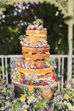 a multi layer cake sitting on top of a table covered in flowers and strawberries