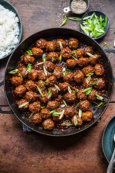 meatballs and rice in a skillet on a wooden table with other food items