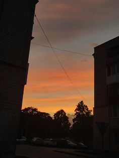 the sun is setting behind some buildings and cars parked on the side of the road