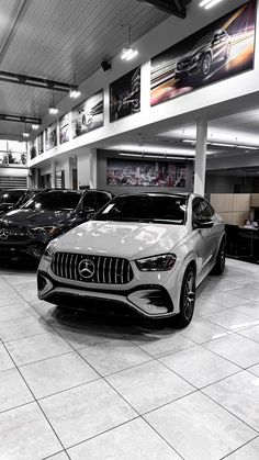 several cars are parked in a showroom with white tile flooring and large windows