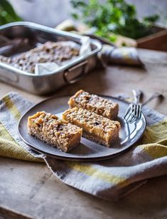 three pieces of cake sitting on a plate with a fork next to it and a pan of food in the background