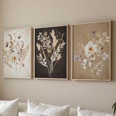 three floral paintings hang on the wall above a white couch