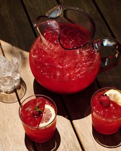 two glasses and one pitcher filled with liquid on a table next to some lemons