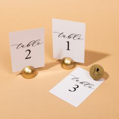 two place cards with gold balls on them next to a corkscrew table number